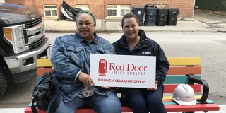 two people sitting on a bench holding a Red Door sign